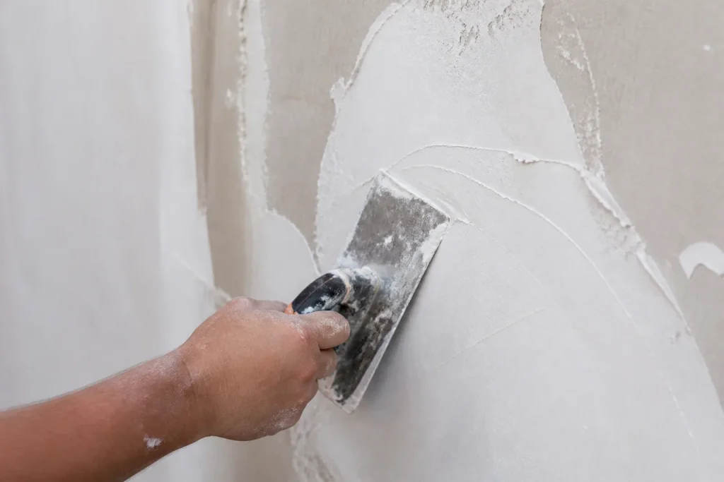 Couteau a enduire tirant un enduit blanc sur mur