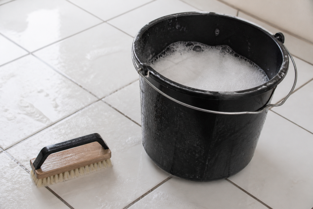 Seau de mousse savonneuse et brosse sur carrelage blanc